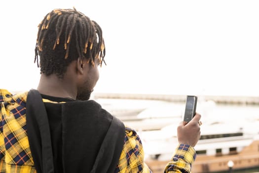 young african man seen from behind taking a picture with his smartphone, lifestyle concept and technology