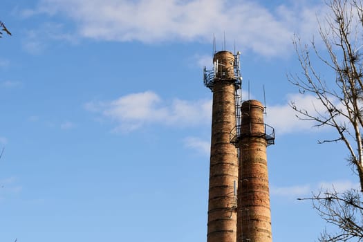 Two tall brick chimneys above abandoned boiler building for venting smoke, combustion byproducts from factory heating. Smokestacks with cell site. Industrial red towers or pipe with mobile antennas