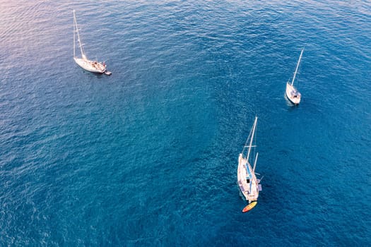 Aerial view of anchored sailing yacht in emerald sea. Aerial view of a boat. Outdoor water sports, yachting. Aerial view of anchoring yacht in open water. Ocean and sea travel and transportation