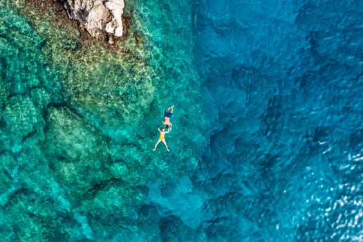 Aerial view of a young couple snorkeling above coral reef reaching deeper parts of the crystal clear water, Rhodes, Greece. Aerial drone view of a couple snorkeling swimming in crystal clear water.
