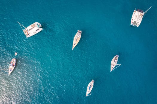 Yacht anchoring in crystal clear turquoise water in front of the tropical island, alternative lifestyle, living on a boat. Aerial view of yacht at anchor on turquoise water, showing luxury, wealth.