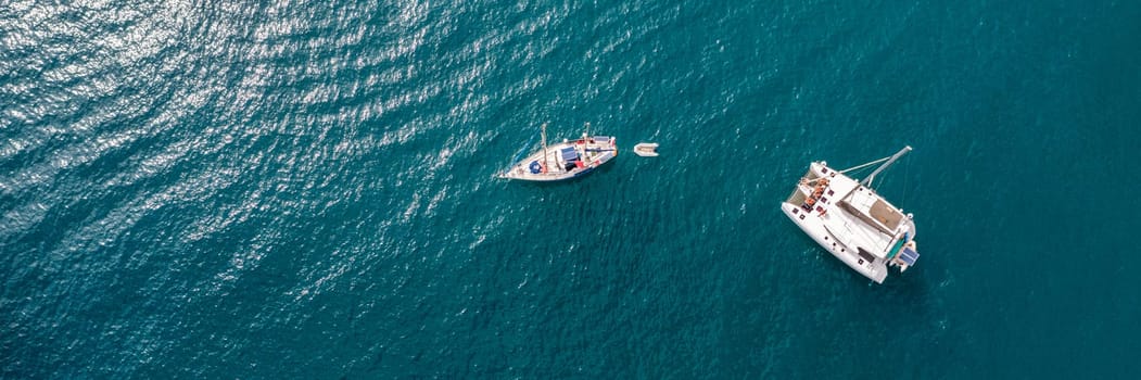 Yacht anchoring in crystal clear turquoise water in front of the tropical island, alternative lifestyle, living on a boat. Aerial view of yacht at anchor on turquoise water, showing luxury, wealth.