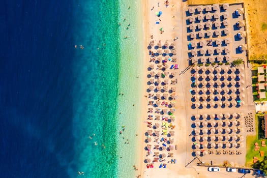 View from above, stunning aerial view of an amazing beach with beach umbrellas and turquoise clear water. Top view on sun loungers under umbrellas on the sandy beach. Concept of summer vacation. 