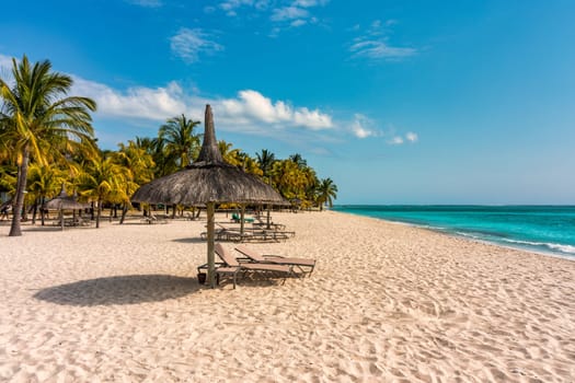 A beach with palm trees and umbrellas on Le morne Brabant beach in Mauriutius. Tropical crystal ocean with Le Morne beach and luxury beach in Mauritius. Le Morne beach with palm trees, white sand and luxury resorts, Mauritius.