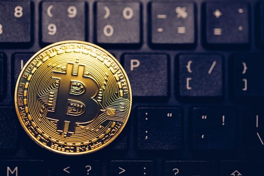 Bitcoin on compuer keyboard in background, symbol of electronic virtual money and mining cryptocurrency concept. Coin crypto currency bitcoin lies on the keyboard. Bitcoin on keyboard.