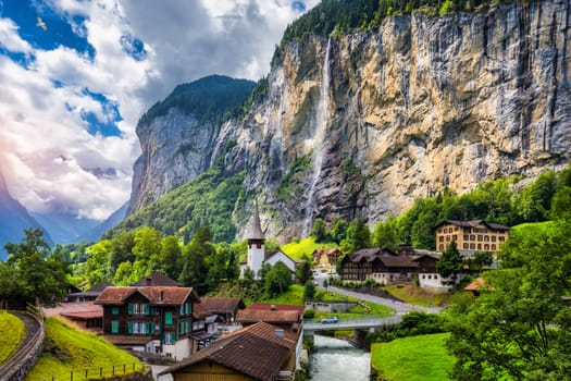 Amazing summer landscape of touristic alpine village Lauterbrunnen with famous church and Staubbach waterfall. Location: Lauterbrunnen village, Berner Oberland, Switzerland, Europe.