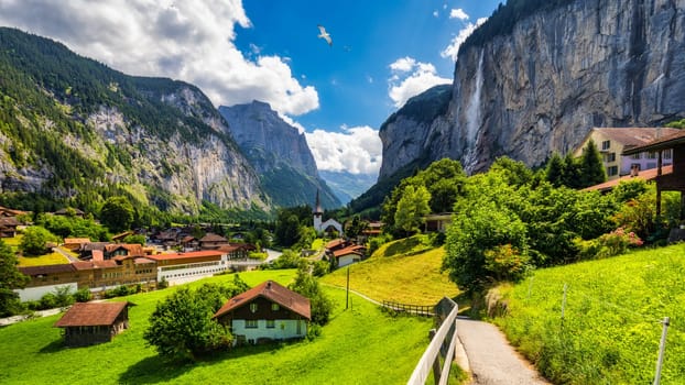 Amazing summer landscape of touristic alpine village Lauterbrunnen with famous church and Staubbach waterfall. Location: Lauterbrunnen village, Berner Oberland, Switzerland, Europe.
