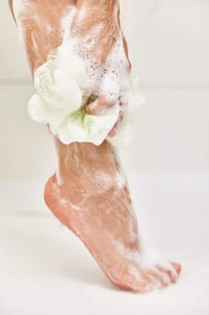 Woman washing her legs with foam bubbles and bath sponge while taking shower in the bathroom