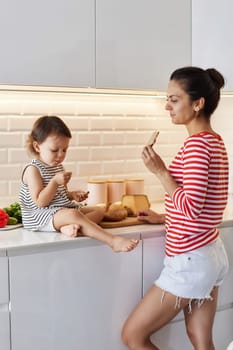happy mother and her cute little girl enjoy preparing breakfast in white kitchen, happy moment together