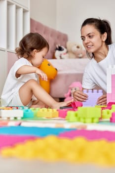 cute baby girl and her loving mother build tower from colorful cubes, having fun together