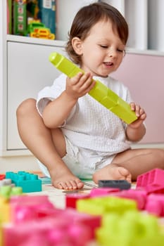 cute baby girl playing with colorful toys bricks at home. kid building green tower