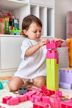 cute baby girl playing with colorful toys bricks in white bedroom