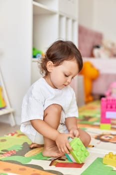 cute baby girl playing with colorful toys bricks in white bedroom