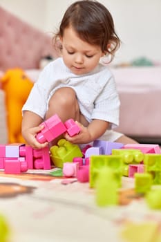 cute baby girl playing with colorful toys bricks at home
