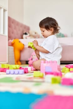 cute baby girl playing with colorful toys bricks in white bedroom