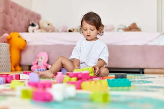 cute baby girl playing with colorful toy blocks at home