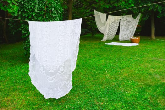 White laundry on clothesline in garden. White curtains drying in the sun