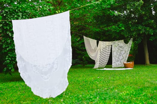 White laundry on clothesline in garden. White curtains drying in the sun