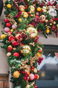 Stylish christmas fir branches with red and gold baubles on front of building holiday market in city street. Winter christmas street decor