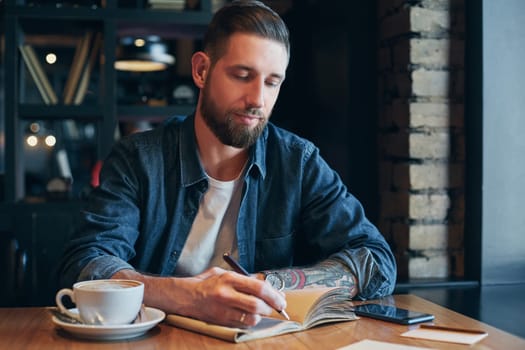 Man hand with pen writing on notebook on a wooden table. Man working at coffee shop