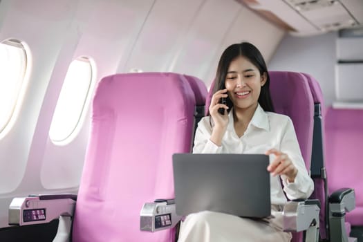 Asian woman using modern smartphone and laptop computer while sitting on airplane Asian woman sitting next to airplane seat window travel and technology.