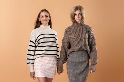 two young women friends hold each other hand walking on beige background