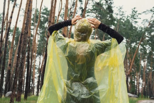 Back view on carefree woman in yellow raincoat walking in autumn forest enjoying rainy weather outdoors. Female tourist discover park in rainy season. Closeness to nature. Mental healing fulfillment clean air