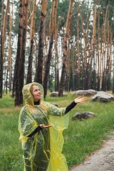 Smiling woman in yellow raincoat walking in autumn forest enjoying rainy weather outdoors. Female tourist discover park in rainy season. Closeness to nature. Mental healing fulfillment clean air