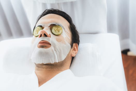 Serene daylight ambiance of spa salon, man customer indulges in rejuvenating with luxurious cucumber facial mask. Facial skincare treatment and beauty care concept. Quiescent