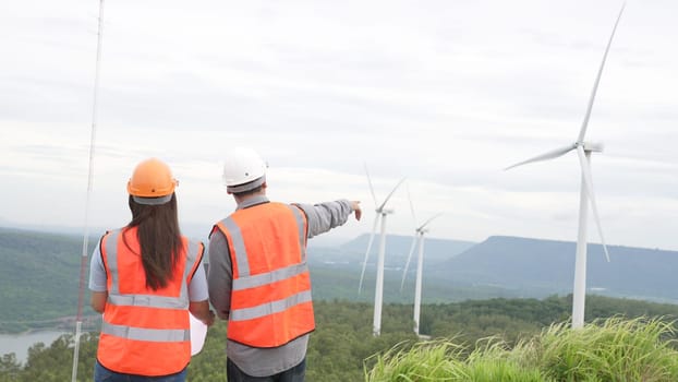 Male and female engineers working on a wind farm atop a hill or mountain in the rural. Progressive ideal for the future production of renewable, sustainable energy.