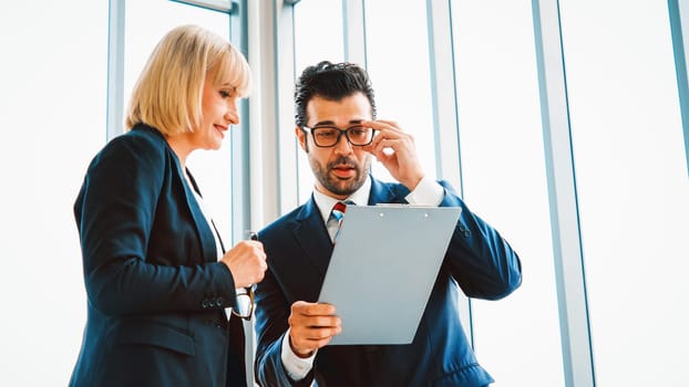 Two business people talk project strategy at office meeting room. Businessman discuss project planning with colleague at modern workplace while having conversation and advice on financial report. Jivy