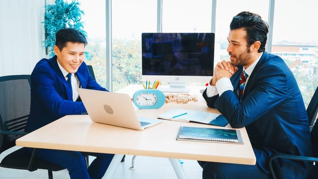 Two business people talk project strategy at office meeting room. Businessman discuss project planning with colleague at modern workplace while having conversation and advice on financial report. Jivy