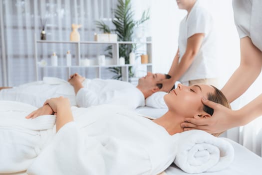 Caucasian couple enjoying relaxing anti-stress head massage and pampering facial beauty skin recreation leisure in dayspa modern light ambient at luxury resort or hotel spa salon. Quiescent