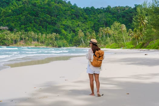 Asian woman with backpack walking at the beach Koh Kood Island Thailand Trat , traveler walking on the beach of the tropical island Ko Kut Island with coconut palm trees on the beach, drone aerial view