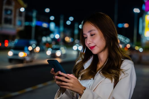 Business woman using mobile phone walking through night city street while waiting car to pick up home, Beautiful young smiling female texting work on smartphone, social media