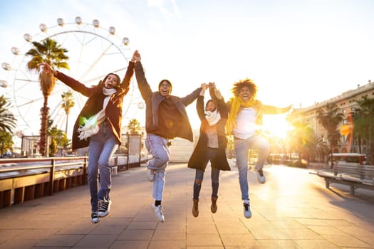 Happy and cheerful multiracial group of friends holding hands jumping mid air in the city on a sunny winter day. Copy space. Celebration concept.
