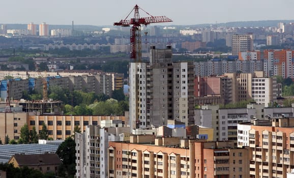 In the heart of an expansive city, a new high-rise building emerges as crane machinery diligently works to shape the urban skyline. Surrounding apartments stand testament to residential life, showcasing a blend of colors and architectural styles.