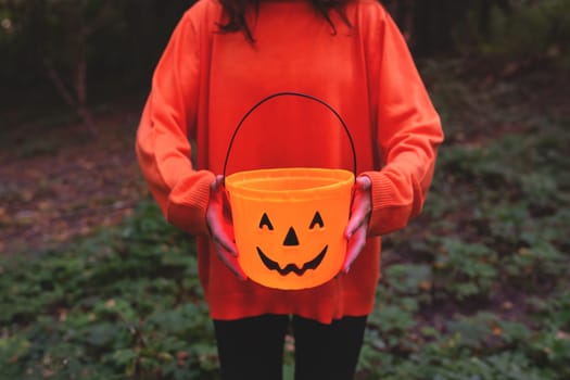 Girl in an orange sweater holding a pumpkin bucket, perfect for autumn and Halloween themes. The image captures the festive spirit with a focus on seasonal celebration and decoration