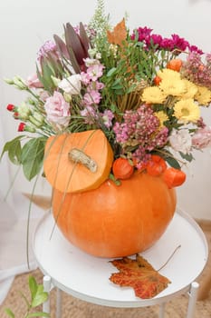 Flower arrangement in a pumpkin, autumn interior decor. Creating handmade autumn decor