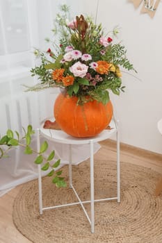 Flower arrangement in a pumpkin, autumn interior decor. Creating handmade autumn decor