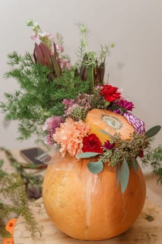 Flower arrangement in a pumpkin, autumn interior decor. Creating handmade autumn decor