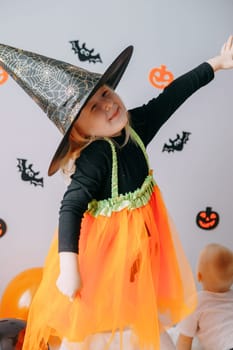 Children's Halloween - a girl in a witch hat and a carnival costume with airy orange and black balloons at home. Ready to celebrate Halloween.