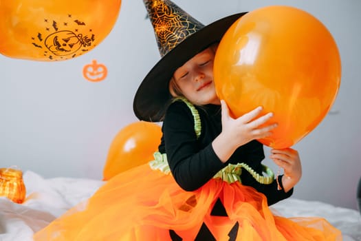 Children's Halloween - a girl in a witch hat and a carnival costume with airy orange and black balloons at home. Ready to celebrate Halloween.