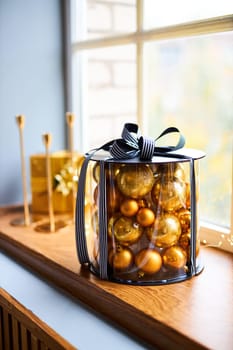 Festively decorated windowsill illuminated by daylight, gift box with golden balls, figurines and candles