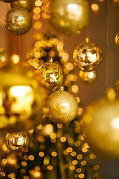 Many large golden Christmas balls look hanging against the background of the Christmas interior. Festive background in golden awards, bokeh, selective focus