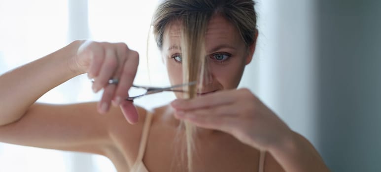 A woman cuts herself a lock of hair, close-up. Doing your own bangs at home during a pandemic. Haircut at home