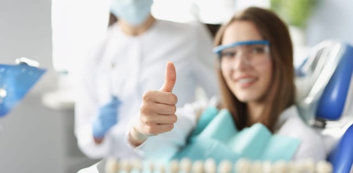 A woman at the dentist shows a thumbs up gesture, blurry, close-up. Professional dental care, satisfied patient