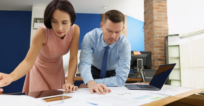 A man and a woman are standing and studying documents on the table, close-up. Collaboration of employees in the office