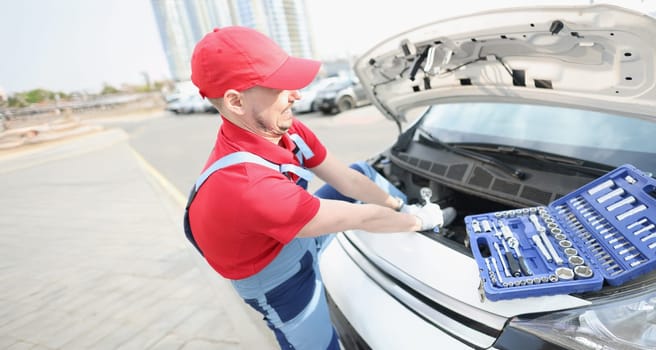 A man in a uniform on the street fixes a breakdown in a car, close-up. Car repair tools, call from repairman