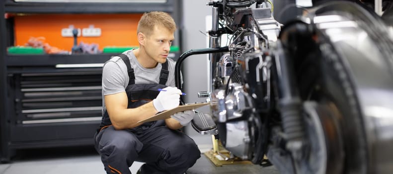A man on a motorcycle takes notes, close-up. Checking the technical condition of the bike in the garage